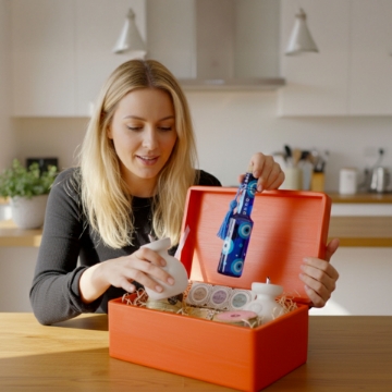 Close-up of a hand placing a bottle of LADOLEA organic extra virgin olive oil inside a red wooden gift crate, highlighting the premium contents. Close-up of a hand placing a bottle of LADOLEA organic extra virgin olive oil inside a red wooden gift crate, highlighting the premium contents.